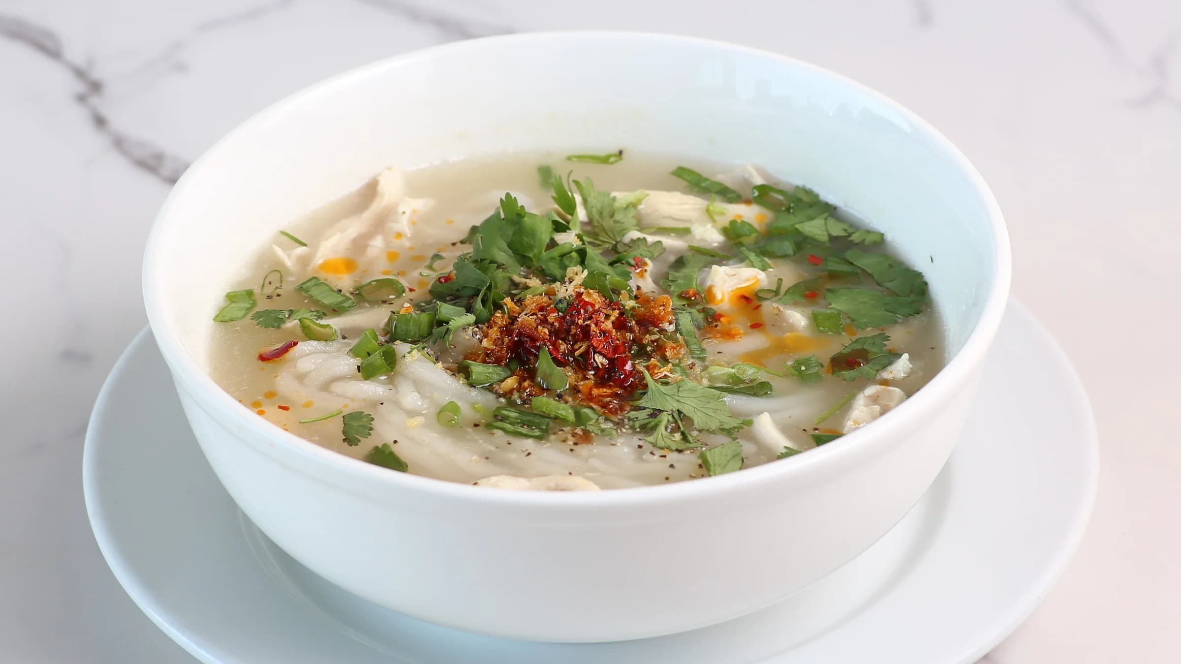 Soft rice noodles in a savory broth, topped with shredded chicken and garnished with fresh herbs, crispy fried shallots, and a drizzle of chili oil.